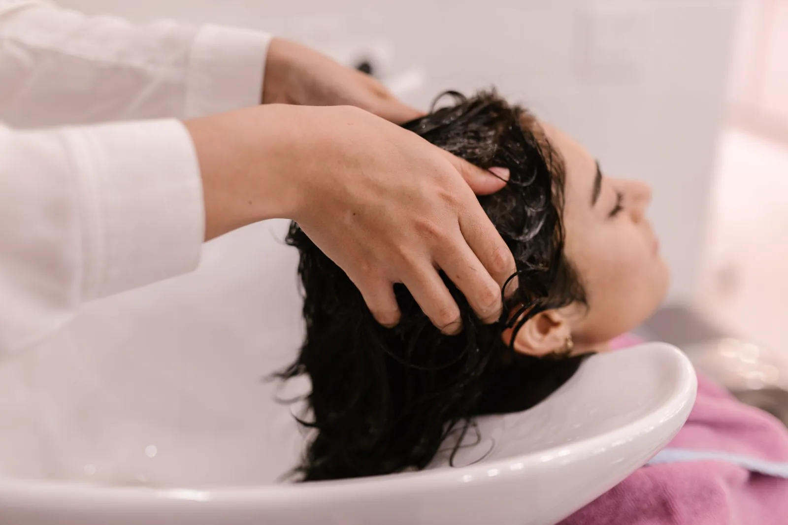 Hands massaging conditioner through wet hair at a salon basin