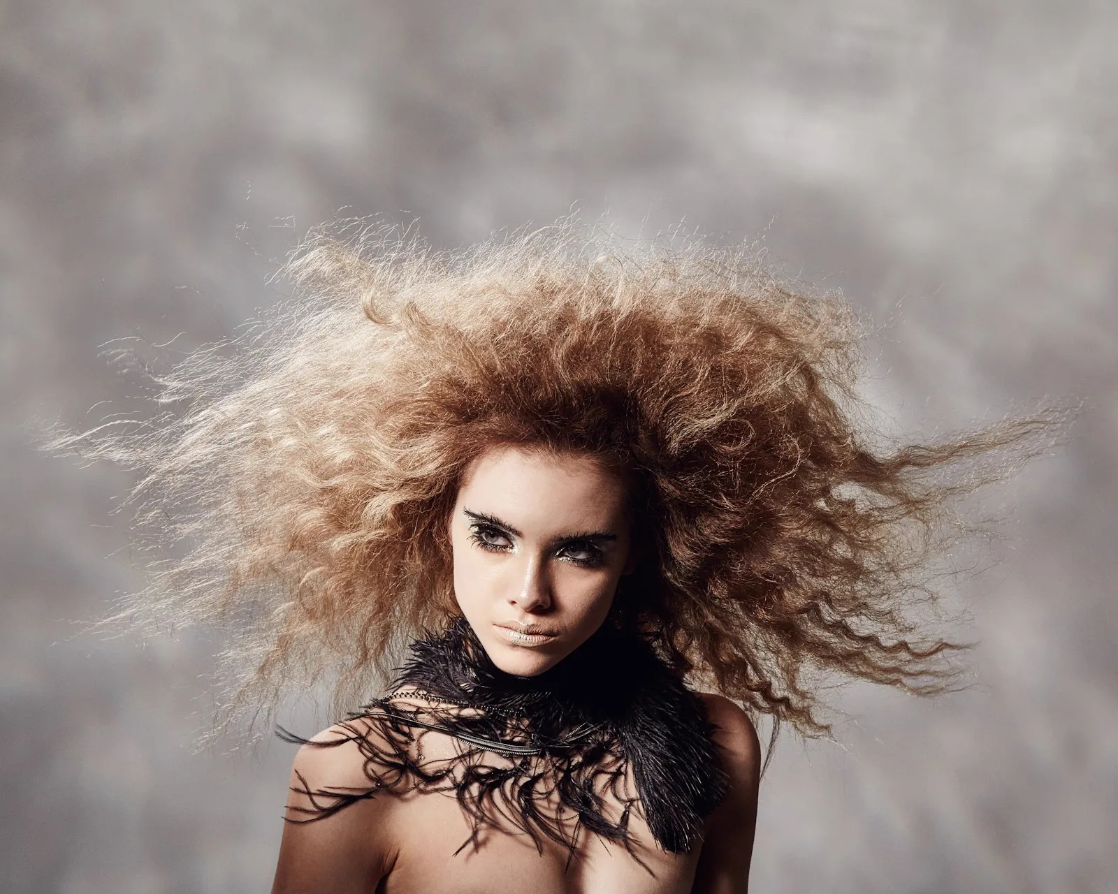 A woman with big, wild, frizzy blonde hair fanned out against a grey studio backdrop