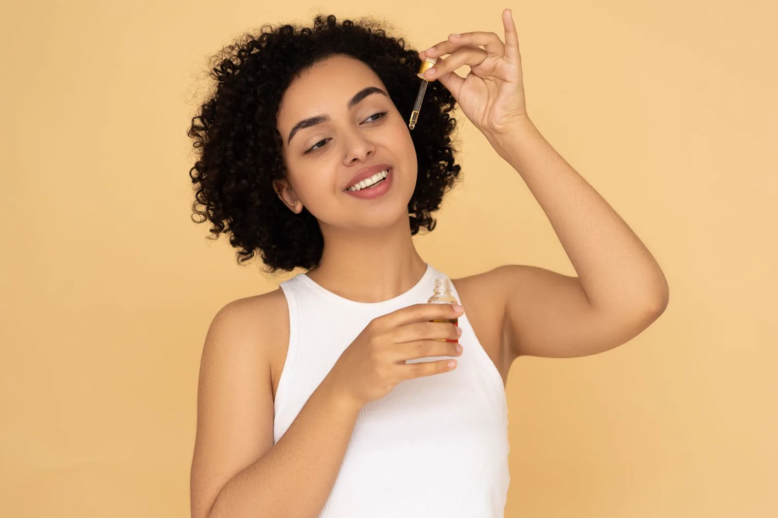 A woman applying hair oil to her curls with a dropper