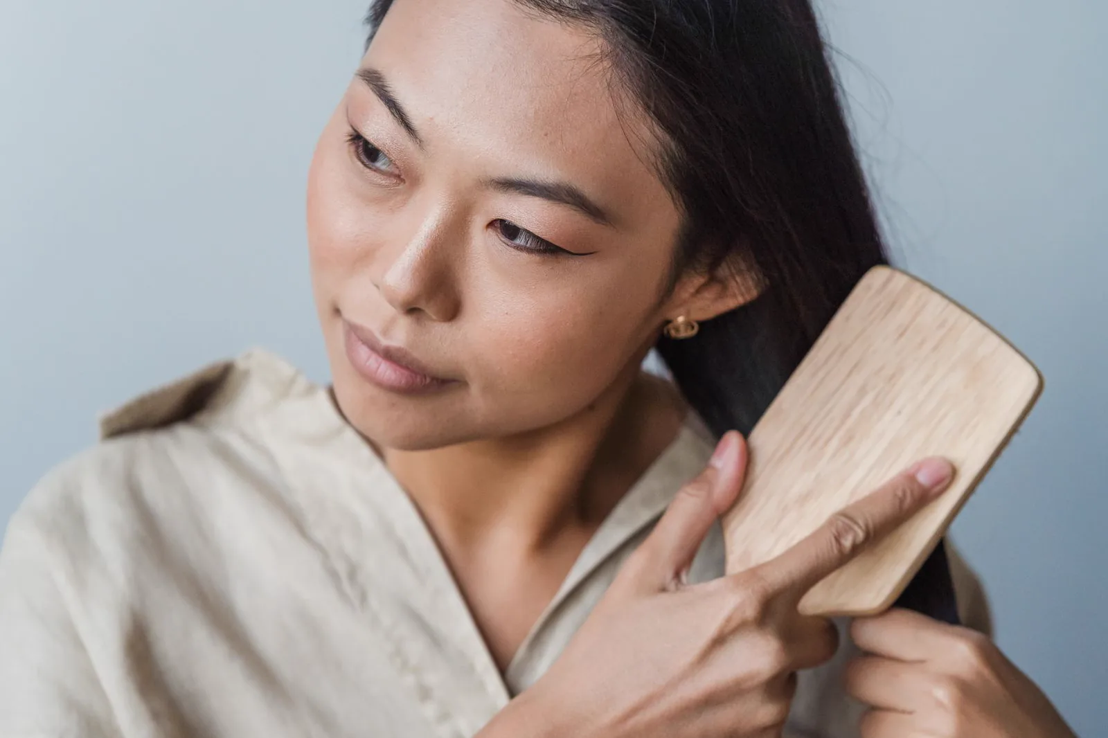 A woman brushing her long, healthy, straight hair with a wooden paddle brush
